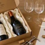 Box vin mariage ouverte sur table en chêne, bouteilles et fiche de dégustation
